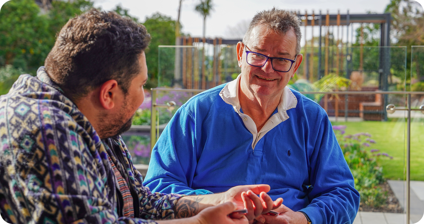 Participant in BrainLink NDIS support program smiling with his carer at a community event outdoors. 